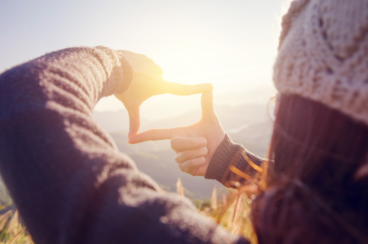 Person a hat with fingers in a square looking toward the horizon